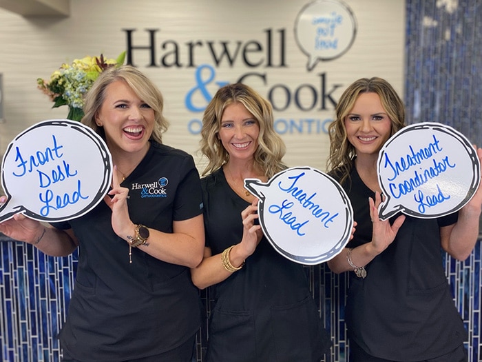Three women holding speech bubble signs. | Harwell & Cook Orthodontics