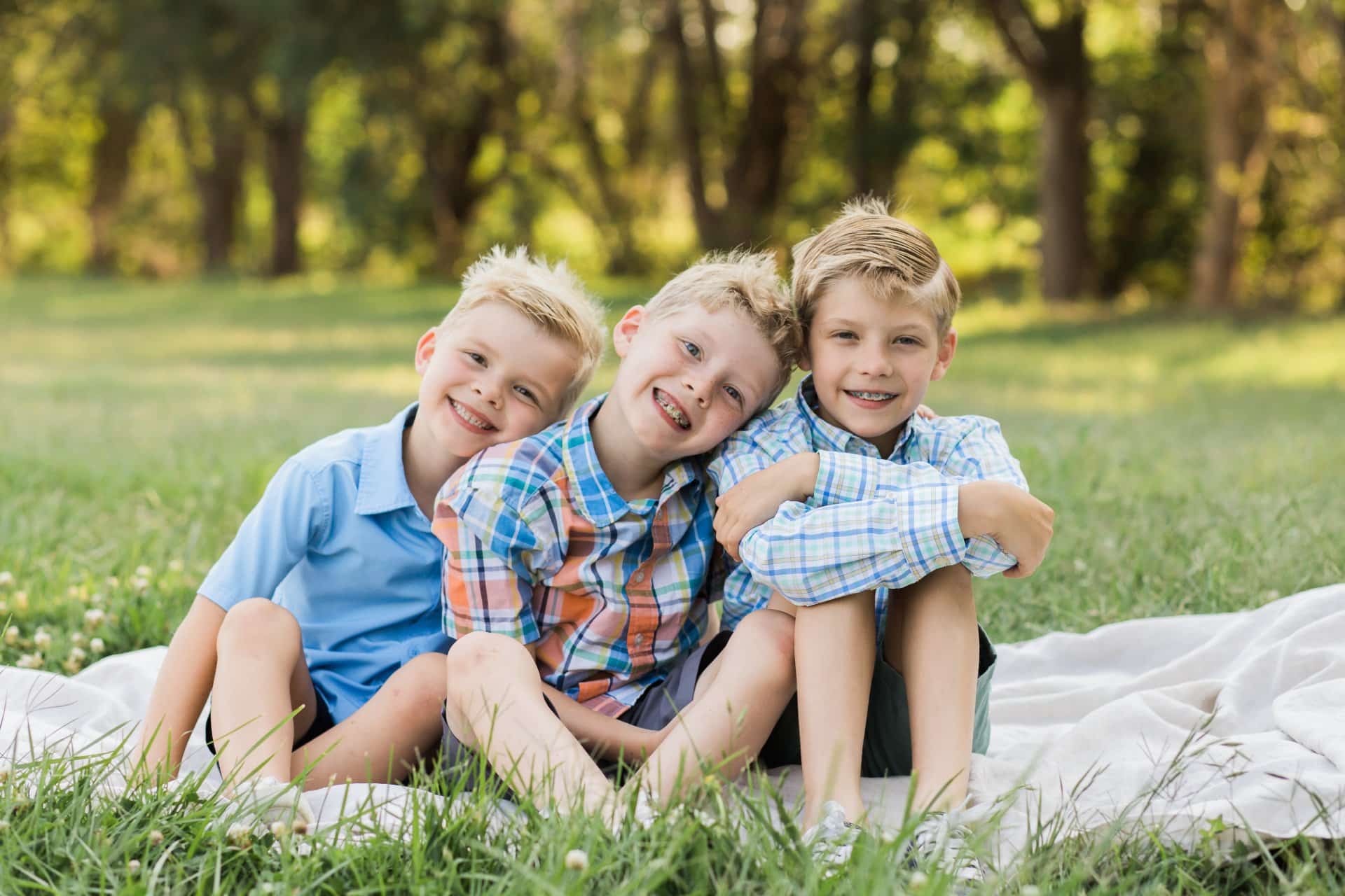 Three boys sitting on the grass. | Harwell & Cook Orthodontics
