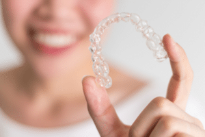 Smiling young woman holding a clear aligner near the camera